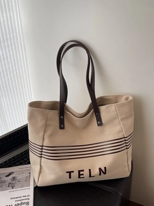 Minimalist canvas tote bag with brown leather handles and striped print on a dark stool