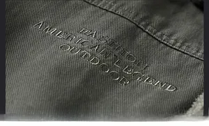 Dettaglio del ricamo e del tessuto in cotone twill pesante sulla giacca outdoor da uomo
