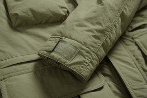 Detail of adjustable velcro cuffs and utility pockets on olive green outdoor jacket