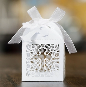 Detailed laser-cut white cross favor box with ribbon on rustic dark wood surface