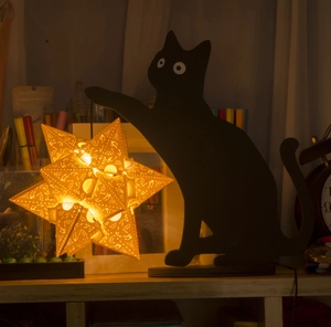 Detailed close-up of a black cat silhouette lamp holding a geometric hollow star light
