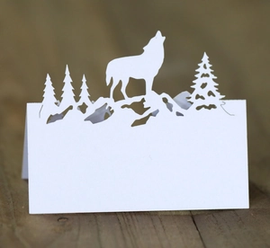 Détail d'un marque-place en papier découpé au laser avec loup hurlant et silhouettes de pins