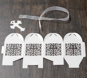 Detailed view of white laser cut cross candy box with ribbon and pendant on wood