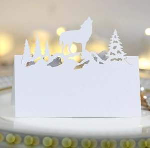 Marque-place blanc découpé au laser avec silhouette de loup et sapins sur une assiette