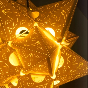 Detail of warm orange laser-cut paper star lantern with intricate whale and moon patterns