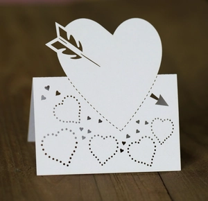 Laser-cut white heart seat card with cupid arrow design on vintage wood surface