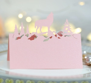 Marque-place rose découpé au laser avec silhouettes de loup et forêt sur assiette blanche