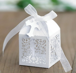 Close-up of laser-cut hollow cross favor box with white satin ribbon and cross tag