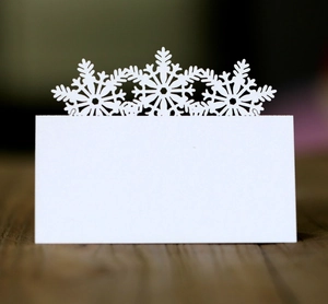 Close-up of laser-cut white snowflake place card on a rustic dark wood table surface