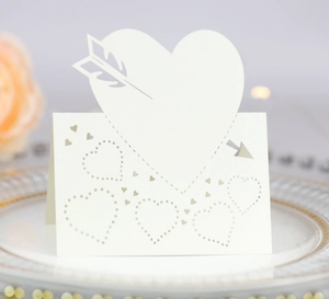 Detail of laser-cut heart and arrow wedding place card on elegant dinner plate