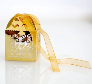 Elegant gold laser-cut candy box with hollow cross design and yellow ribbon for weddings