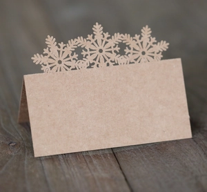 Detail of laser-cut snowflake kraft paper place cards on a dark wood table