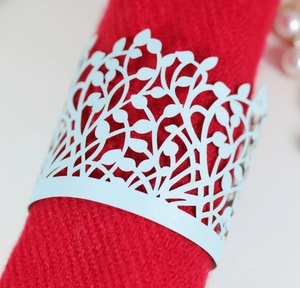 Close-up of light blue laser-cut napkin ring with intricate leaf pattern on red fabric