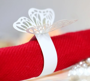 Detail of white laser-cut butterfly paper napkin ring on a elegant red cloth napkin