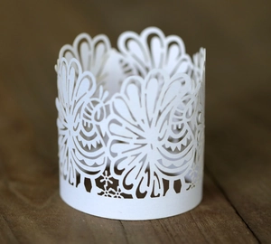 Laser-cut white paper candle holder wrap with intricate feather and petal patterns
