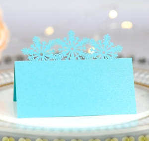 Close-up of light blue laser-cut snowflake place card with glitter finish on a white plate