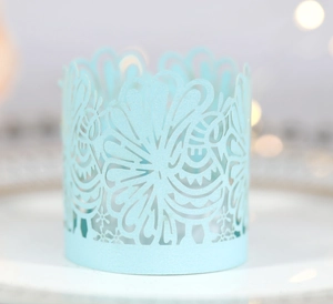Light blue laser-cut lace paper candle cover with elegant floral patterns on a white plate