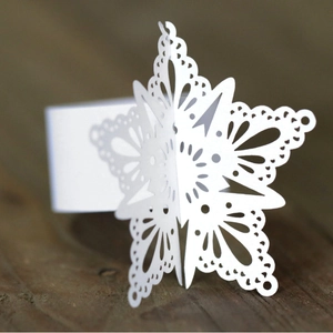 White laser-cut snowflake napkin ring with intricate lace detail on rustic wood background