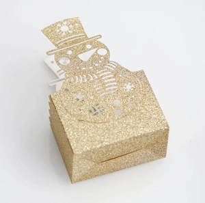 Close-up of golden glitter gift box featuring a cutout snowman design for Christmas
