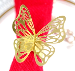 Detailed close-up of a gold butterfly napkin ring with hollow patterns on red fabric