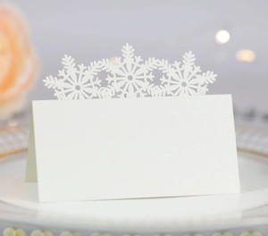 Close-up of laser-cut snowflake crowns on white pearlescent place cards for Christmas