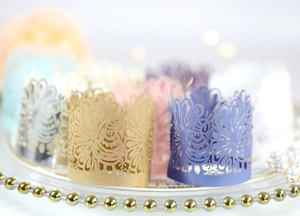 Intricate laser-cut cupcake wrappers in various pearlescent colors on a glass tray