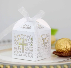 Macro shot of white laser-cut wedding favor box with cross pattern and ribbon bow