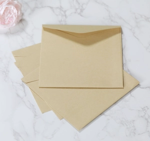 Close-up of square kraft paper envelopes on marble surface with decorative pink rose