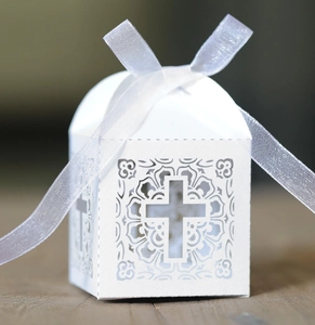 Close-up of white laser-cut wedding favor box with cross design and satin ribbon