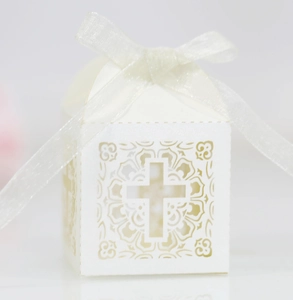 Close-up of laser-cut cross design on white pearl candy box with a sheer ribbon bow
