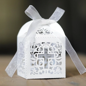 Macro detail of laser-cut white cross favor box with delicate hollow floral patterns