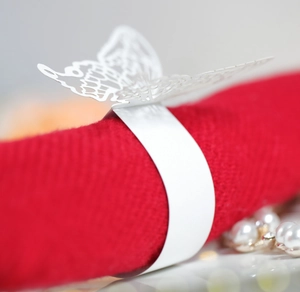 Detail shot of a white laser-cut butterfly napkin ring on a red cloth with pearls