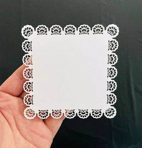 Detailed view of white square paper doilies with laser-cut floral lace patterns for crafts