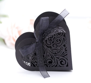 Macro detail of laser-cut vine patterns on a black heart-shaped gift box with a silk bow