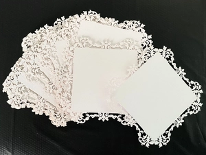 Detailed macro view of laser-cut white lace paper cards with intricate floral vine patterns