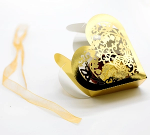 Detail of laser-cut heart-shaped gold candy box with intricate floral patterns and ribbon
