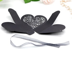 Flat lay of laser-cut heart pattern wedding candy box with elegant black ribbon detail