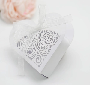 Close-up of white heart-shaped favor box with laser-cut lace and silk bow detail