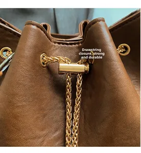 Detail of brown leather bucket bag featuring a gold chain drawstring and sturdy metal eyelets