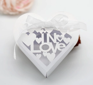 Detail of white laser-cut wedding favor box featuring IN LOVE hollow heart pattern
