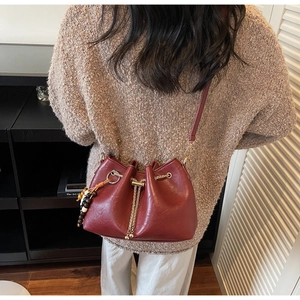 Burgundy bucket bag with drawstring closure featuring elegant chain and beaded charm detail