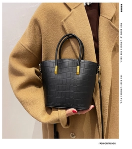 Detail of black crocodile texture bucket bag with gold hardware held by model in coat