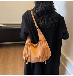 Detail of brown suede hobo bag with tassel accents on a model in a black blazer