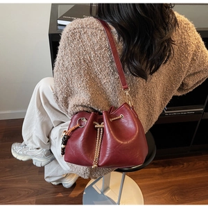 Detail of burgundy drawstring bucket bag with gold chain and beaded tassel charm