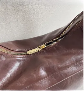 Detailed close-up of a smooth gold metal zipper on a dark brown leather shoulder bag