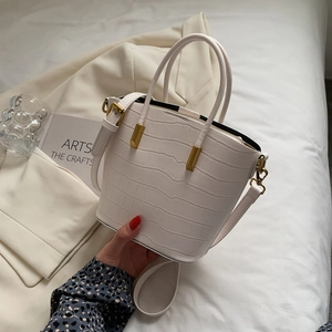 Detail of white crocodile embossed bucket bag with gold hardware and top handle strap