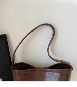 Gros plan sur la bandoulière lisse et le sac seau brillant en similicuir marron foncé