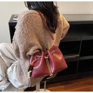 Detail of burgundy drawstring bucket bag with gold chain and ethnic wood bead charm
