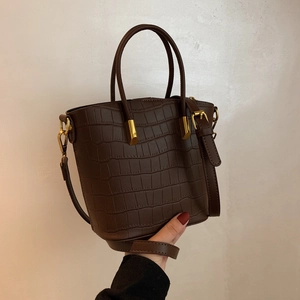 Detail of dark coffee crocodile pattern leather bucket bag with gold metal hardware