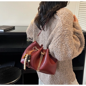 Detailed view of burgundy bucket bag with wooden bead charm and metal drawstring chain